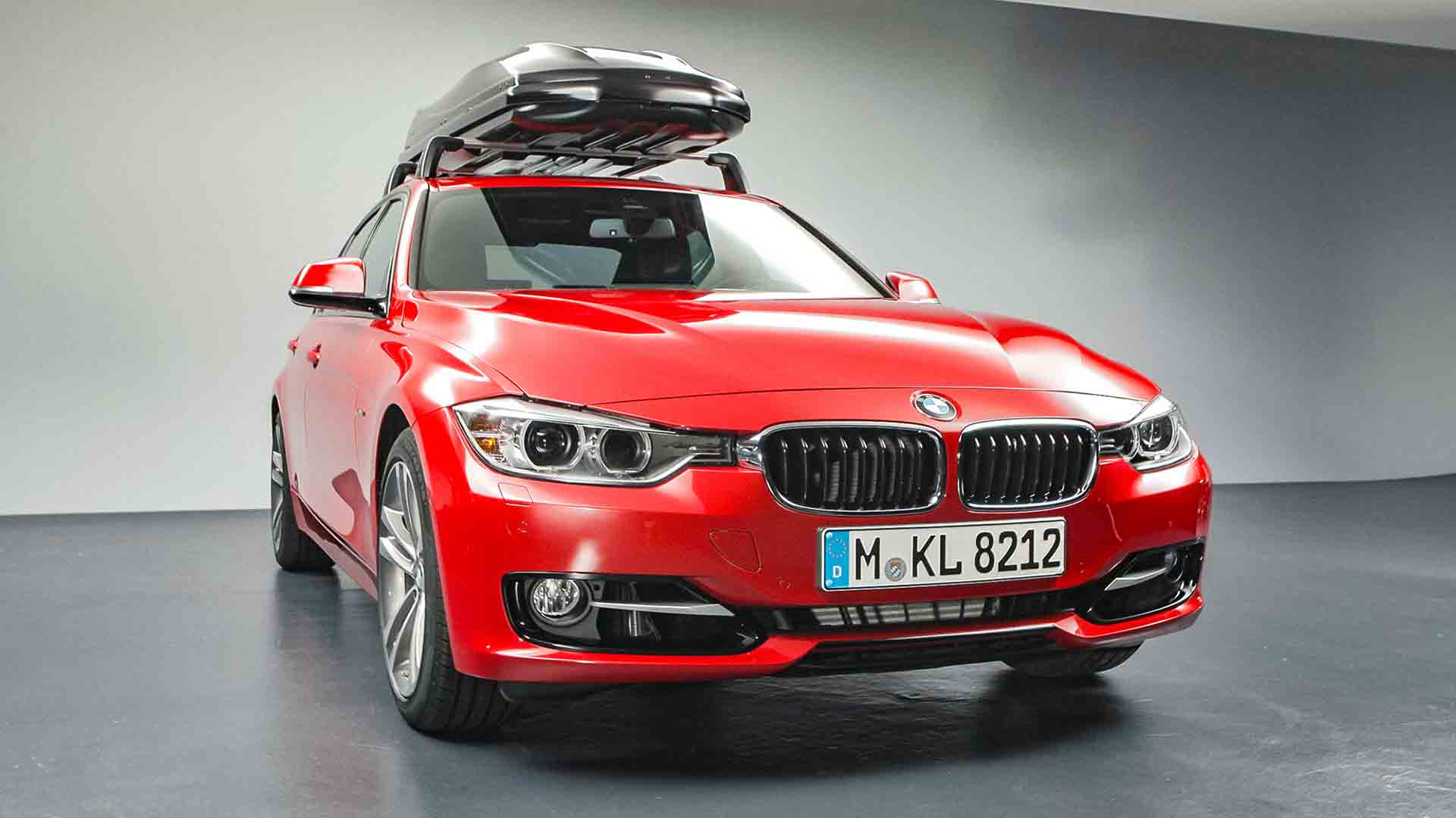 Das Bild zeigt ein Auto. Es ist ein roter BMW, der einen Gepäckträger auf seinem Dach hält. Man sieht ihn von vorne, sein Kennzeichen zeigt die Nummer M-KL 8212. Das Bild dient als Sliderbild für den Portfolioeintrag BMW F30 Zubehör von Panda Pictures.